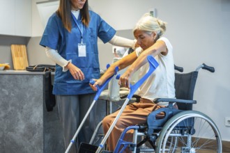 Professional caregiver assisting an elderly woman from a wheelchair, supporting her as she prepares