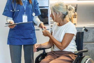 Nurse handing blister pack medication to a senior woman in a wheelchair at home, illustrating