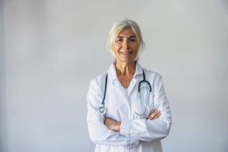 Senior female doctor with gray hair and a lab coat smiling confidently, standing against a neutral