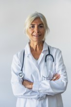 Senior woman doctor with gray hair and lab coat standing confidently with arms crossed, stethoscope