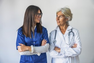 Two confident female doctors, one younger and one older, standing with crossed arms against a white
