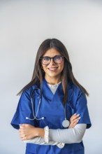 Young woman doctor wearing blue scrubs, a stethoscope, and eyeglasses, standing confidently with