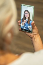 Senior woman holding smartphone for a telemedicine video call with doctor, receiving virtual