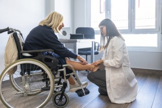 Doctor examining a patient's leg and ankle, the patient sitting in a wheelchair during a