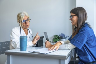 Experienced doctor discussing treatment with a smiling young nurse, both utilizing digital tablets