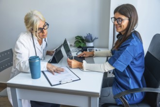 Female physician and junior nurse collaborate in a modern clinic office, reviewing patient data on