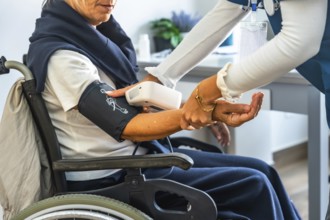 Healthcare professional measuring blood pressure of an elderly woman in a wheelchair, providing
