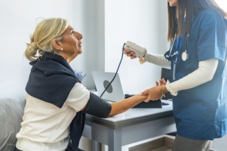 Young medical professional in blue scrubs carefully checking the blood pressure of a smiling senior