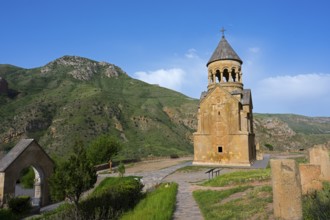 A chapel against a green mountain landscape under a blue sky, surrounded by nature, Noravank