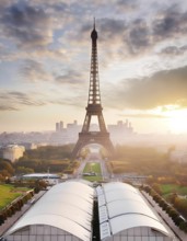 The Eiffel Tower is a tall structure in the background of a city. The sky is cloudy and the sun is