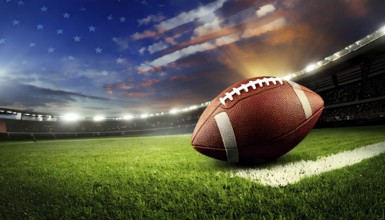 American football ball resting on a vibrant green field, illuminated by stadium lights, ready for