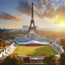 A large green field with a stadium in the background. The stadium is surrounded by trees and