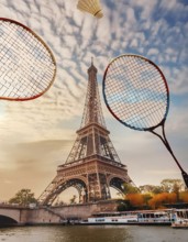 Two tennis rackets are in the air above the Eiffel Tower. The sky is cloudy and the sun is setting,