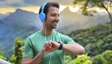 A man wearing headphones and a green shirt is smiling and looking at his watch. He is wearing a