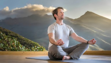 A man is sitting on a mat in front of a mountain. He is meditating and looking up at the sky, AI