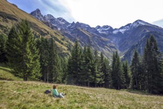 Young woman sitting in a meadow and looking at the mountains of the Allgäu Alps with