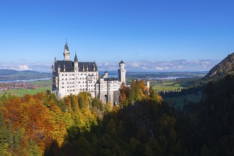 Fairytale castle Neuschwanstein on a wooded hill surrounded by autumnal splendor under wide skies,