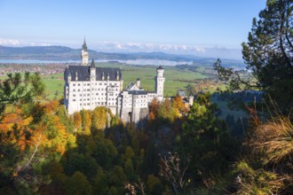 Fairytale Neuschwanstein Castle surrounded by autumnal forest and blue sky in picturesque