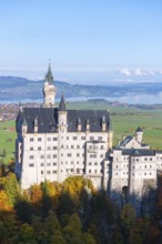Neuschwanstein Castle on wooded hill across valley with majestic panorama and autumnal colors,