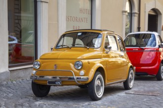 A yellow Fiat 500 is parked in an alley in central Rome
