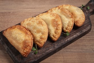 Fried chebureks, deep-fried, mini, on a chopping board, wooden table, close-up, no people