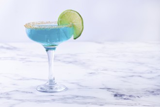 Bright blue cocktail with a slice of lime on a marble surface