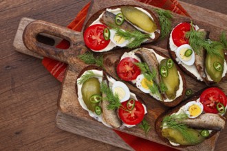 Sandwiches on rye bread with sprats, quail eggs, fresh tomatoes and pickled cucumber, on a wooden