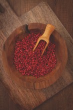 Bright red peppercorns, in a wooden bowl, with a small wooden tray