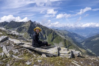Person sitting on a rock with a view of mountain landscape under blue sky, Valais Alps, Valais,