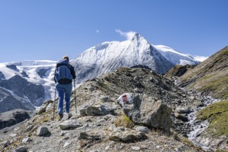 Female hiker with hiking sticks on a rocky slope with a view of snow-covered mountain peaks, Mont