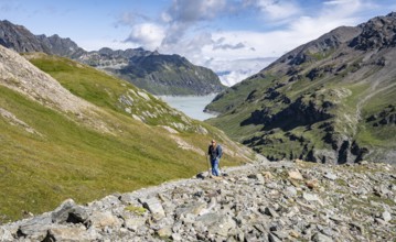 Hiker in a wide mountain landscape with a view of valley and lake, surrounded by green hills, Mont