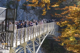 Group of people on Marienbrücke near Neuschwanstein, surrounded by autumn trees and rocks,