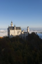 The spectacular Neuschwanstein Castle rises above autumn hills and sea of clouds, Schwangau near