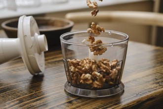 A person is preparing to chop walnuts using a food processor in a cozy kitchen. The walnuts are