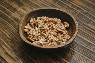 Bowl filled with shelled walnut pieces on a wooden table in a cozy kitchen setting