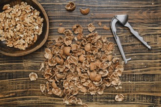Walnuts are being shelled on a rustic wooden surface. A bowl of walnut pieces sits nearby, while