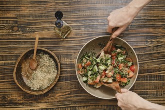 Two hands mix fresh vegetables in a bowl while preparing a salad. Nearby, a smaller bowl holds