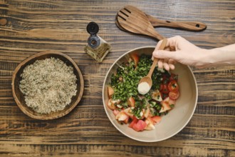 A hand adds seasoning to a bowl filled with chopped tomatoes and fresh herbs in a cozy kitchen