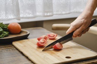 A person is slicing ripe tomatoes on a wooden cutting board with a sharp knife. Bright sunlight
