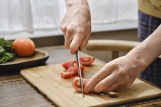 Hands skillfully slice fresh tomatoes on a wooden cutting board while preparing a delicious meal in