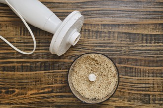 A food processor on a wooden countertop, with finely ground walnuts in the mixing bowl. The scene