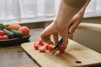 A person is skillfully slicing ripe cherry tomatoes on a wooden cutting board in a bright kitchen.