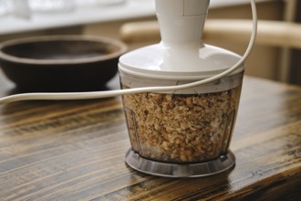 Chopping walnuts in a food processor on a rustic wooden table. The device is plugged in and the