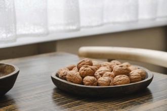 A wooden bowl filled with fresh walnuts on a rustic table in a bright, airy kitchen. Soft natural