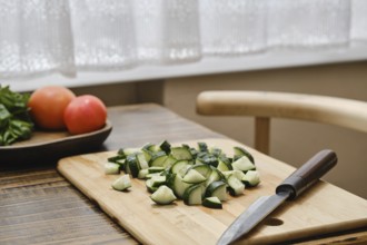 Freshly chopped cucumbers on a wooden cutting board beside a knife. A bowl of tomatoes is visible