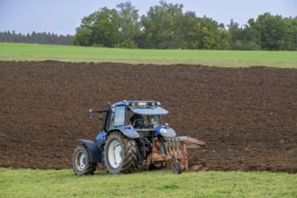 Tractor with plough, agricultural ploughing machine working on a field in autumn, fall in the