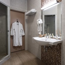 Fine hotel bathroom interior in beige color with bathrobe hanging on the door