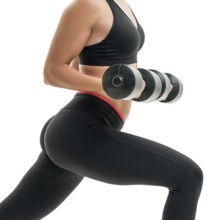 Pretty fitness trainer in black top and leggings exercising with dumbells in studio isolated photo