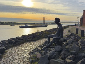 Photo with melancholy mood of bronze sculpture Poortekerl looking at Rhine waiting for ship to