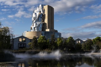 Front lake with artificial fog, Luma, 56 m high irregular tower designed by Frank Gehry, tower in